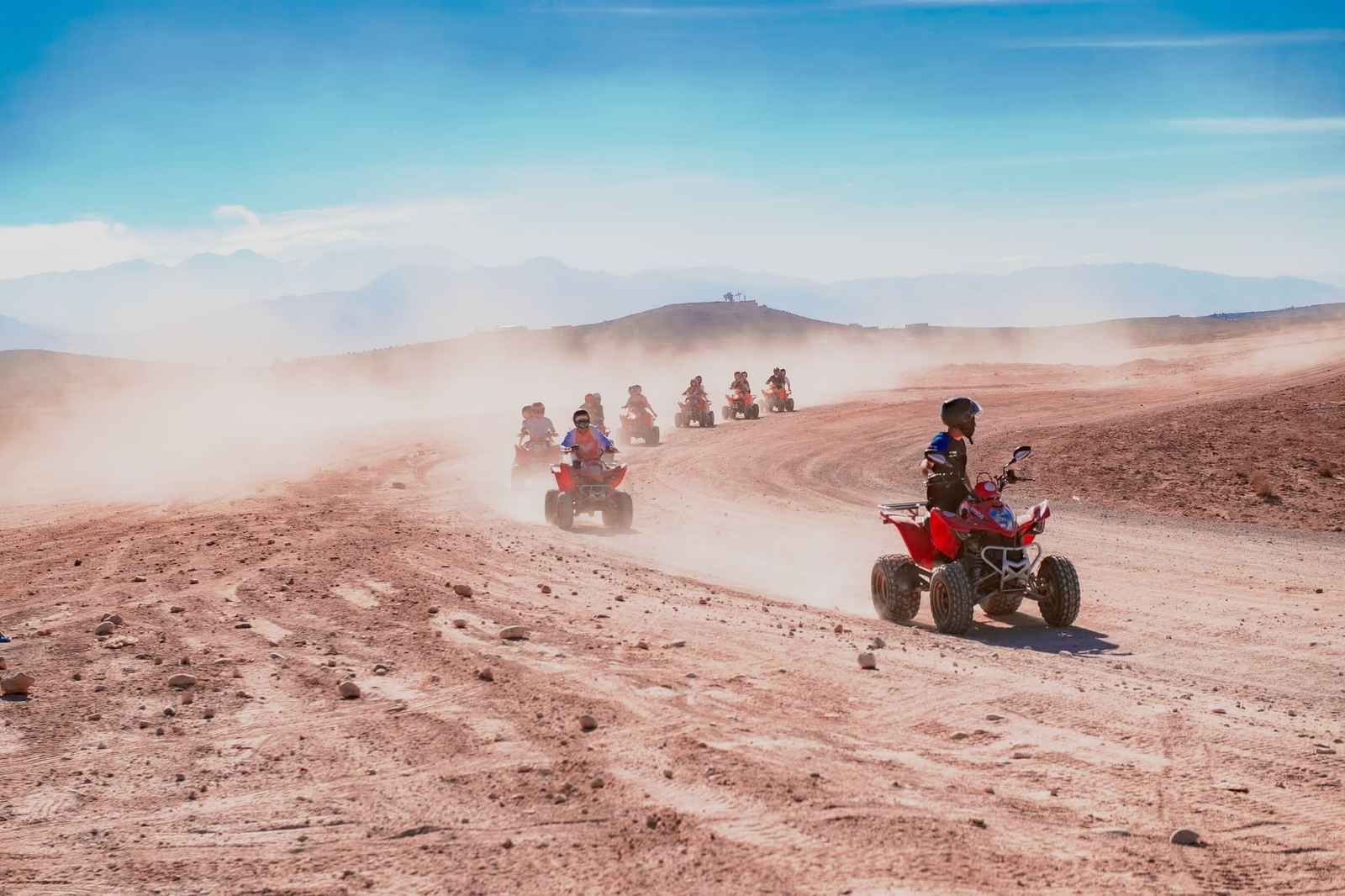 Column of quads raising dust on an Agafay track, hills in the background