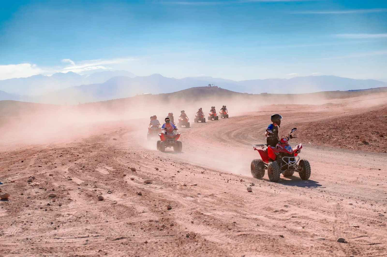 Column of quads raising dust on an Agafay track, hills in the background