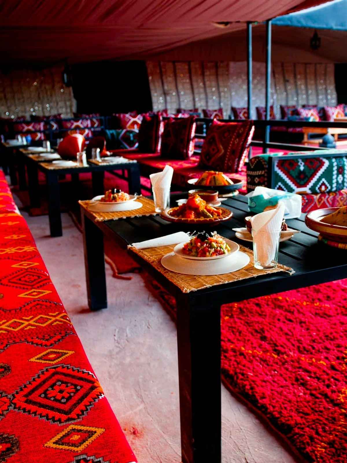 Tables laid with tajines and salads, red benches and rugs under the tent