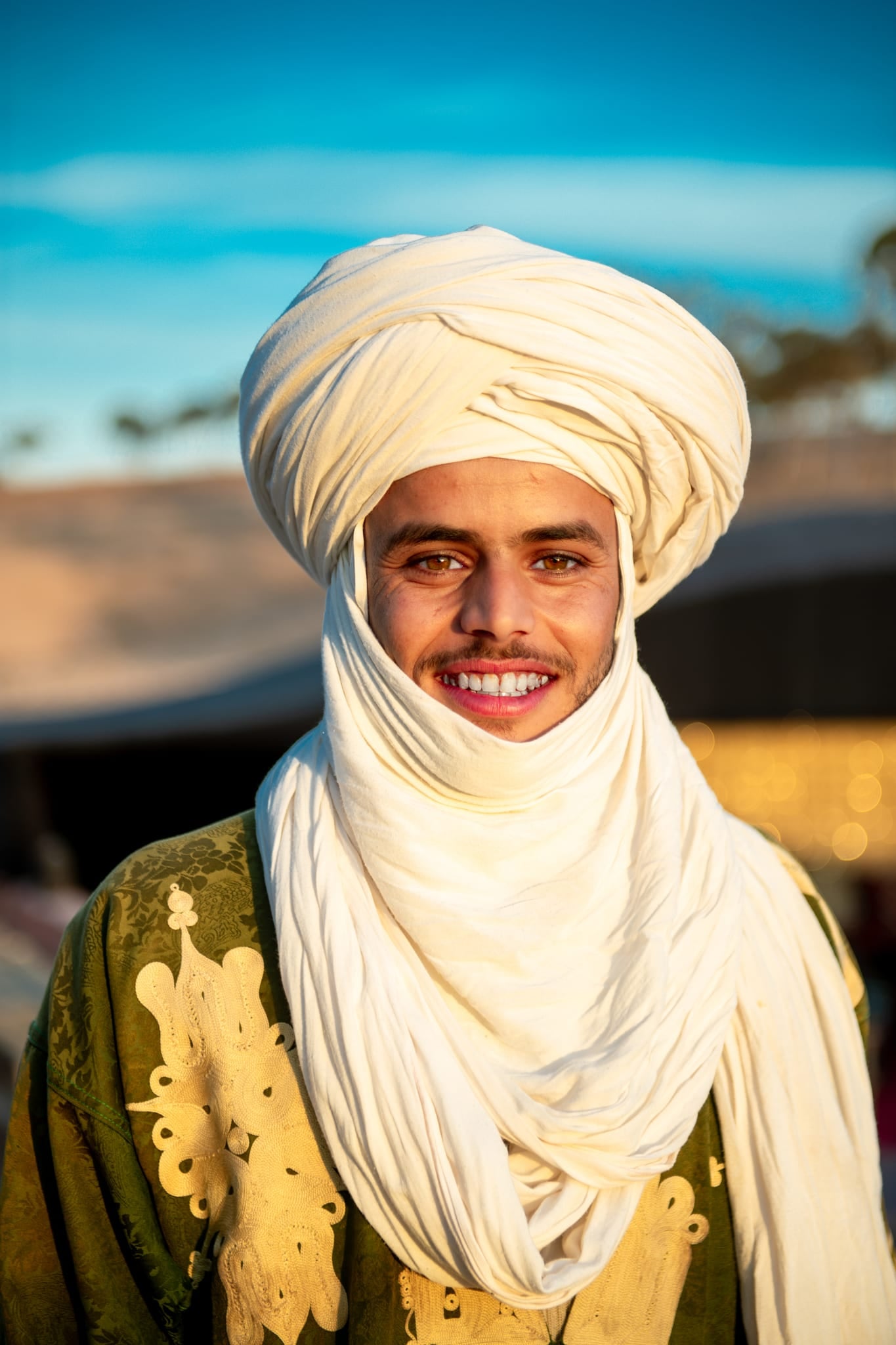 Ein lächelnder Mann mit weißem Turban und besticktem Gewand im Camp in der Agafay-Wüste