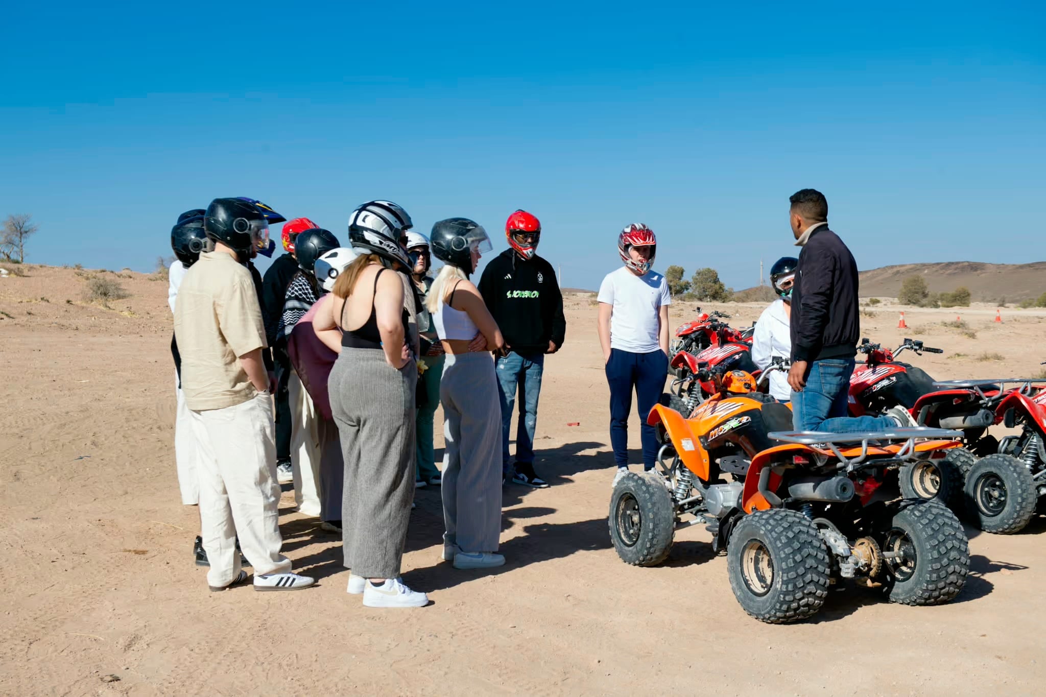 Piloti con il casco riuniti accanto ai quad prima della partenza
