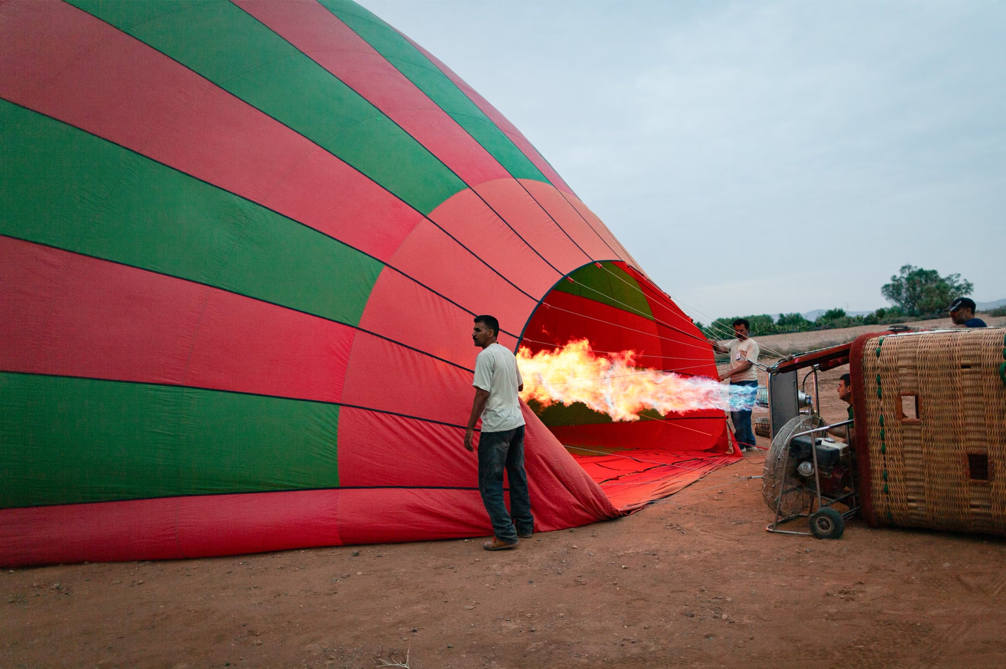 Pilot neben einem rot-grünen Ballon, der am Boden liegt und von der Flamme des Brenners mit heißer Luft gefüllt wird