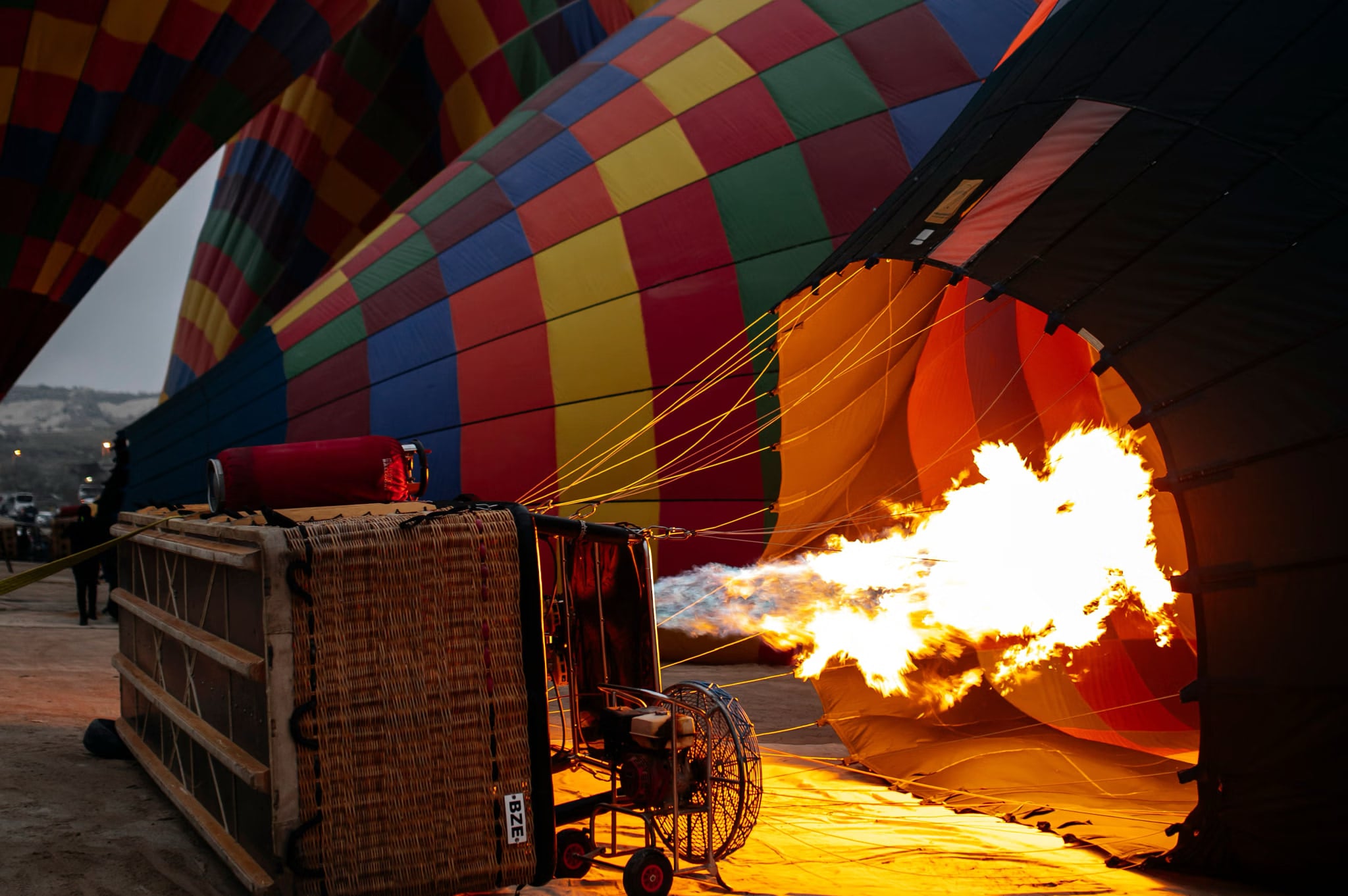 Fiamma del bruciatore sparata dentro una mongolfiera a patchwork rossa, gialla e blu, la cesta coricata davanti