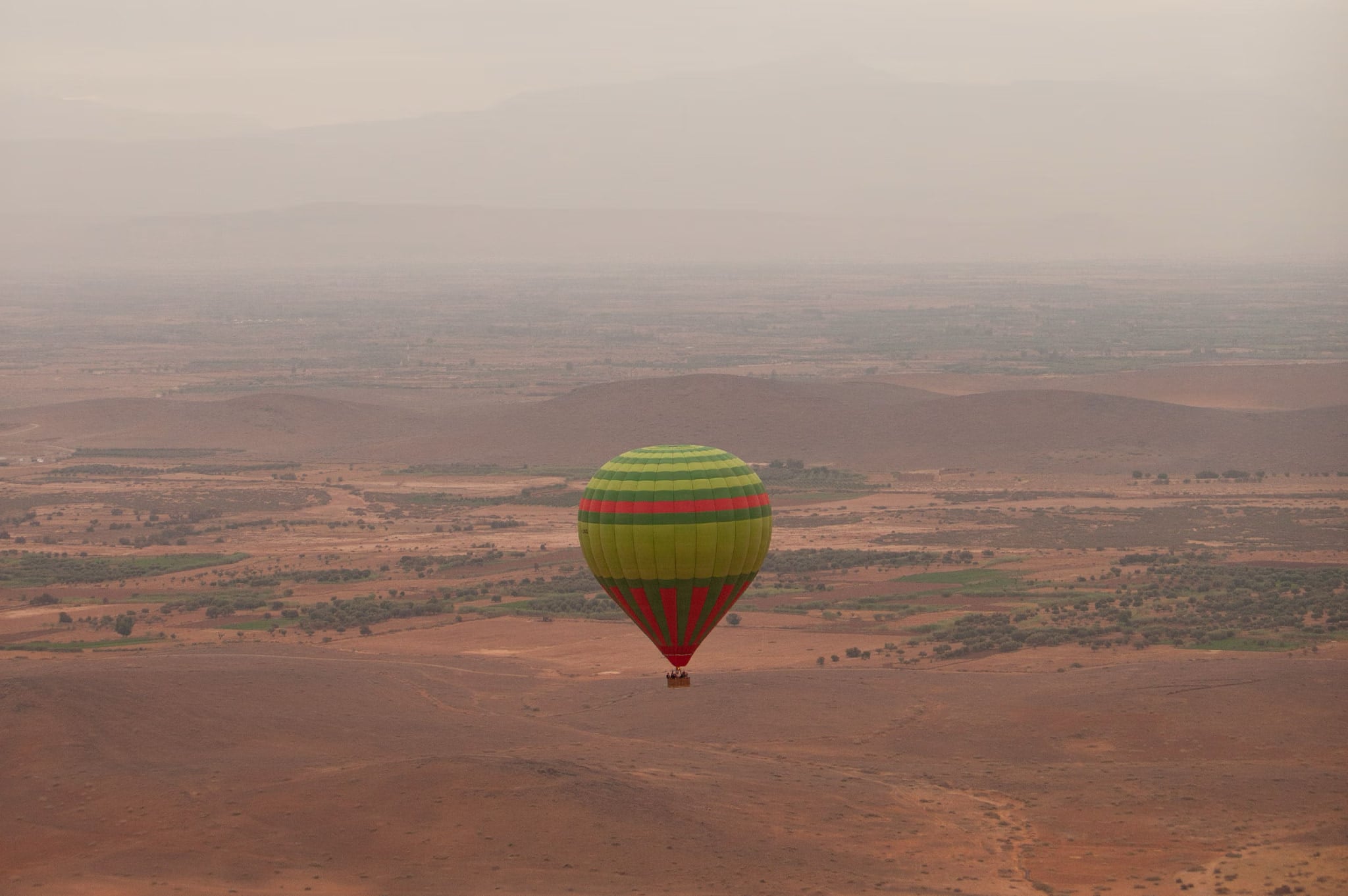Una mongolfiera a strisce che scivola bassa sopra la pianura vicino a Marrakech, nella luce velata del mattino