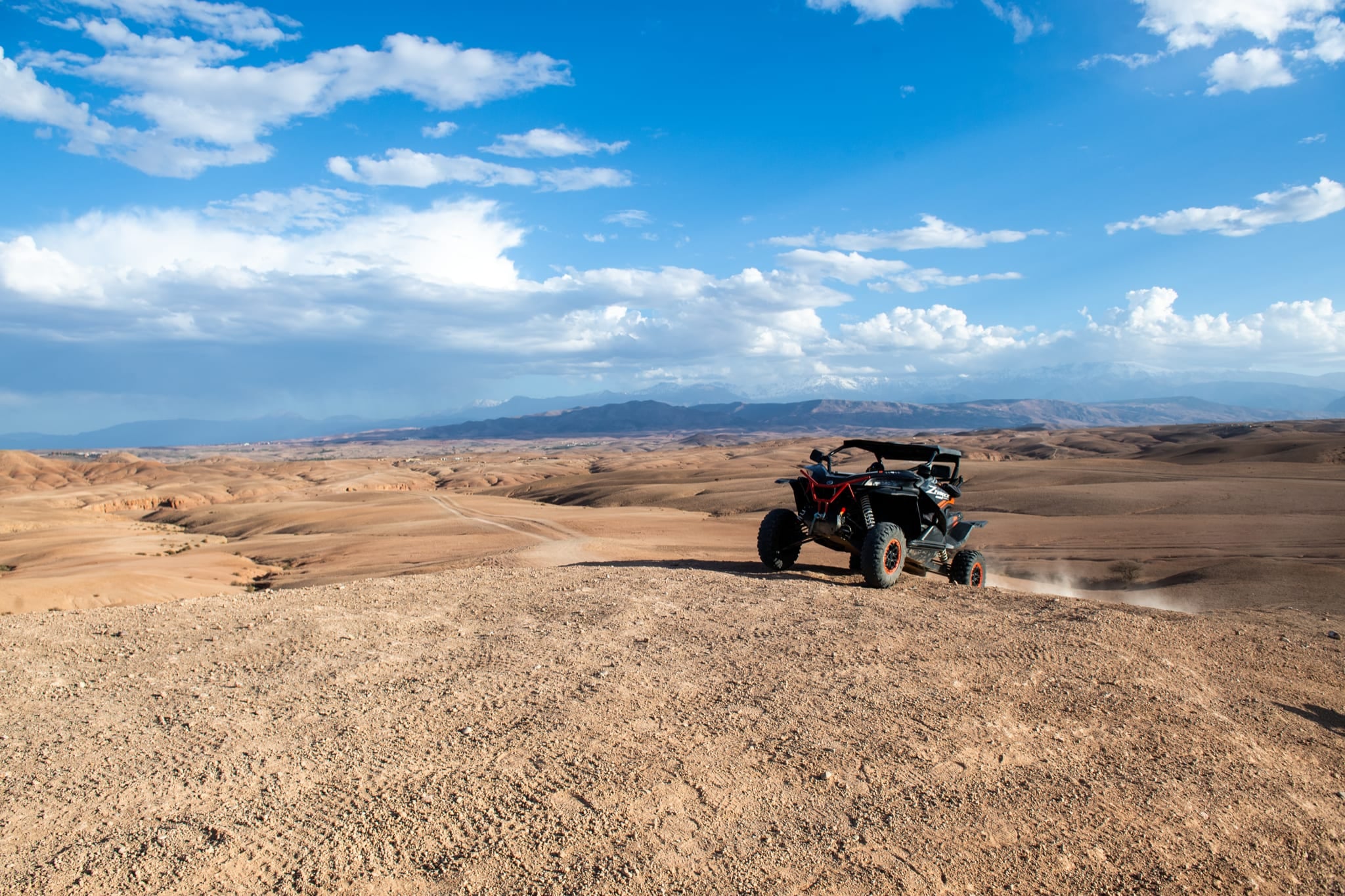 Buggy nero sul bordo di un altopiano, le colline di Agafay più in basso e l'Atlante all'orizzonte