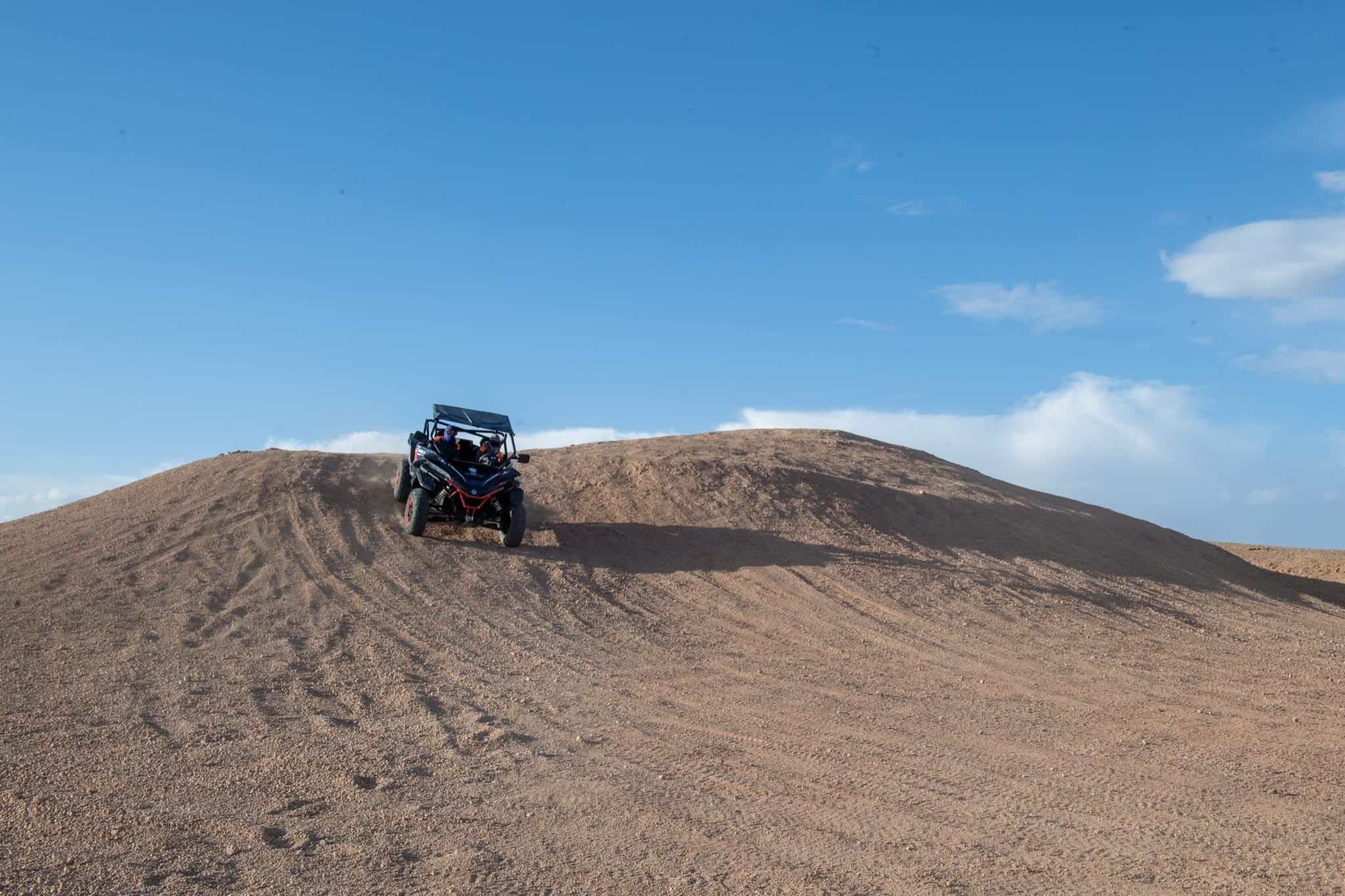 Buggy rijdt langs de kam van een aarden heuvel naar beneden, onder een strakblauwe lucht