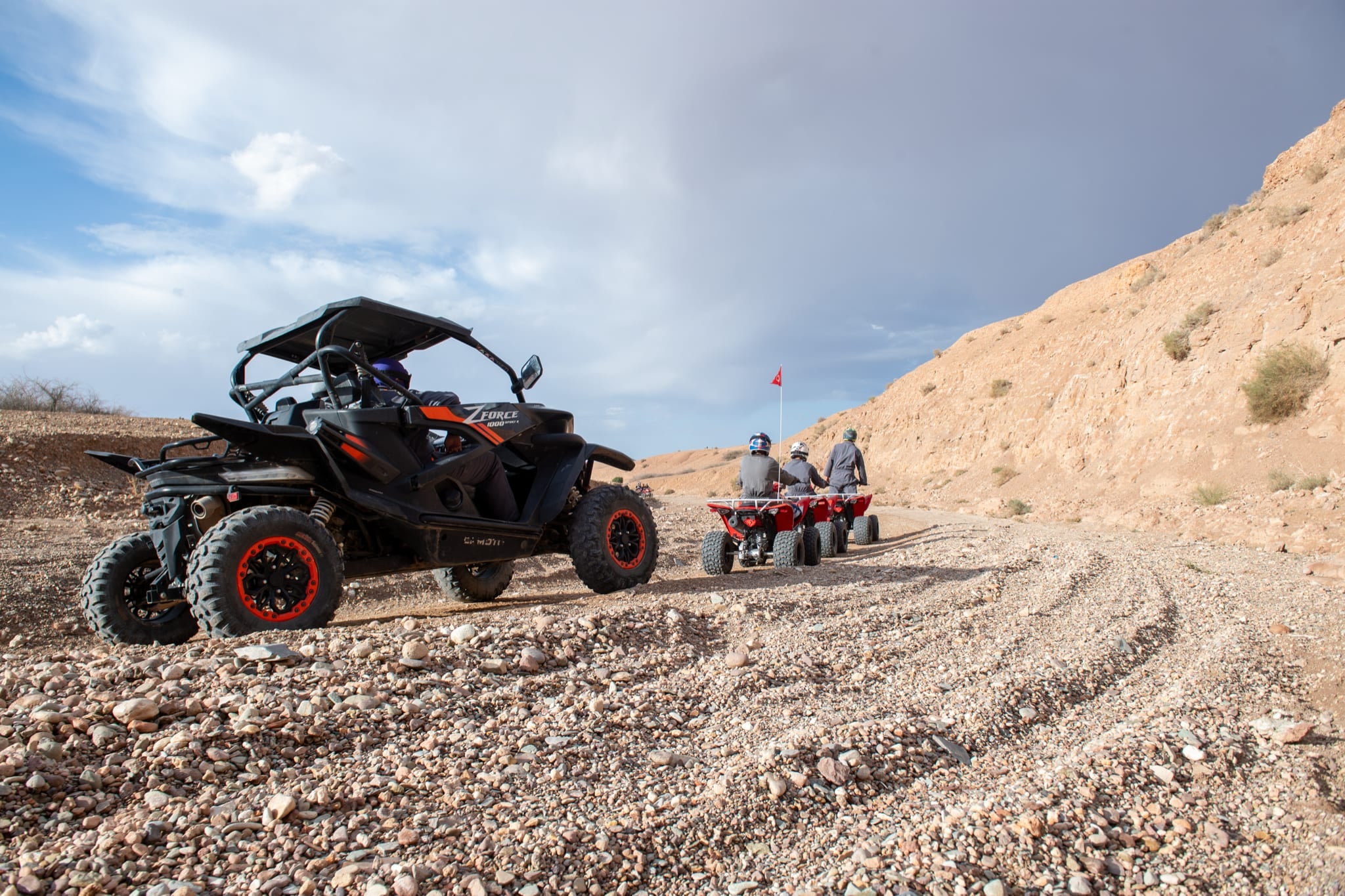 Buggy nero fermo su una pista sassosa mentre una fila di quad rossi si allontana verso una bandierina