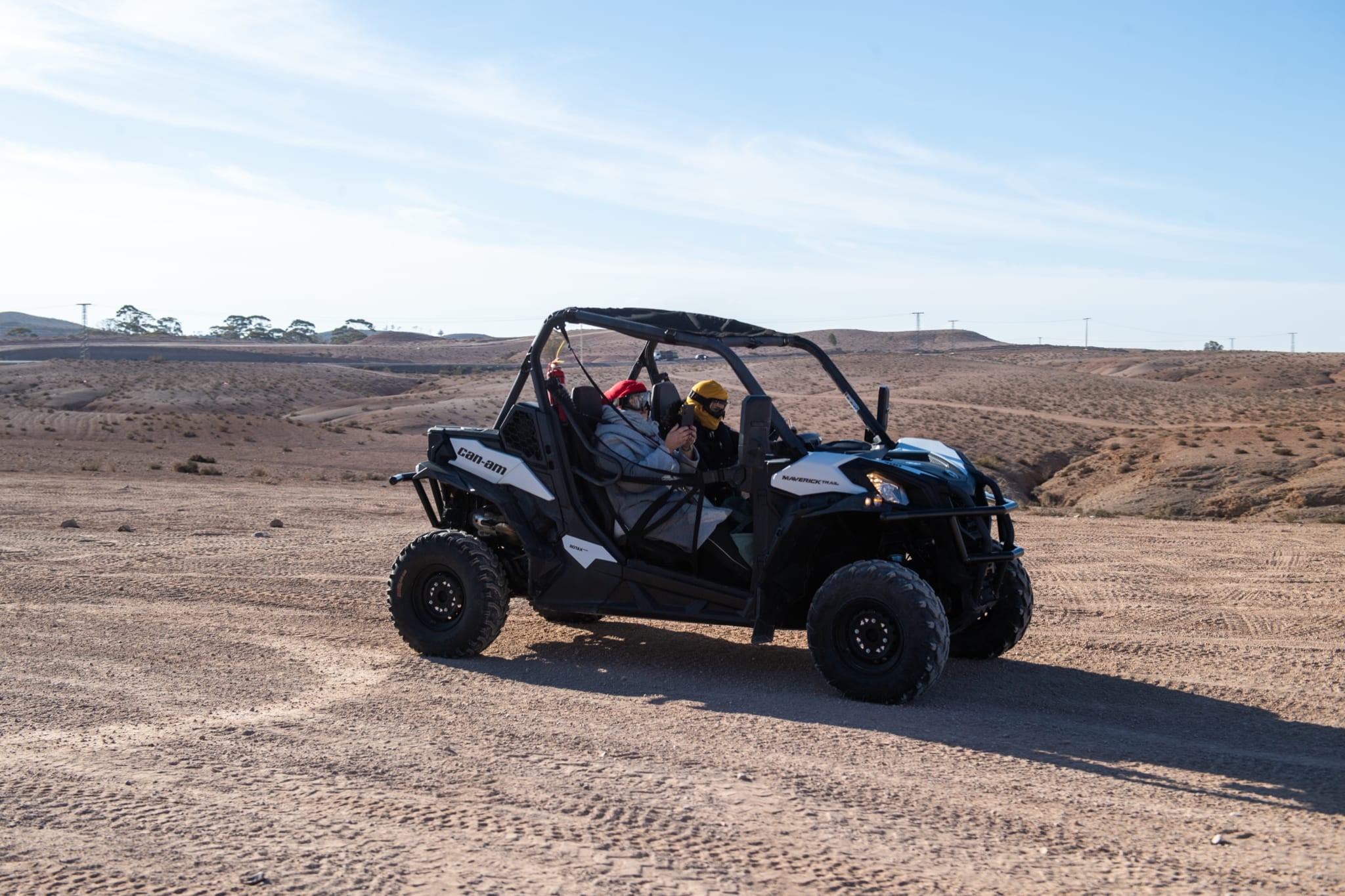 Buggy bianco e nero con due persone a bordo in un tratto pianeggiante del deserto, una filma con il telefono
