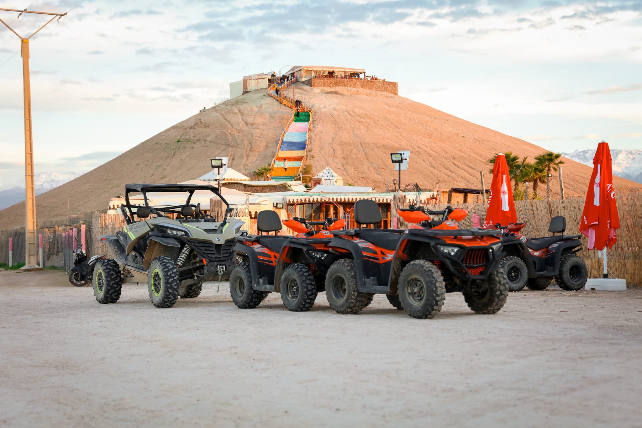 Quads und ein Buggy am Fuß der Düne, eine bunte Treppe führt nach oben