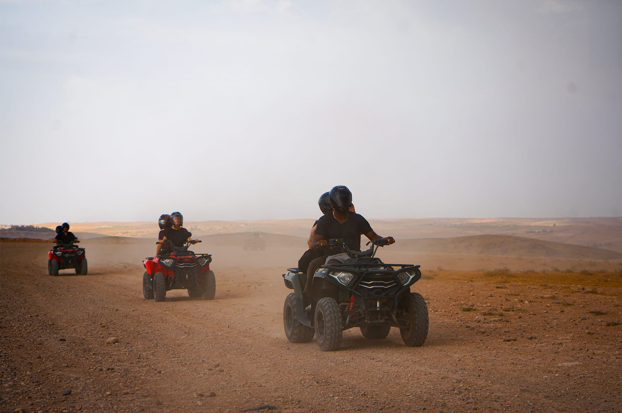 Drei Quads mit Fahrern und Beifahrern durchqueren ein staubiges Stück der Agafay-Wüste