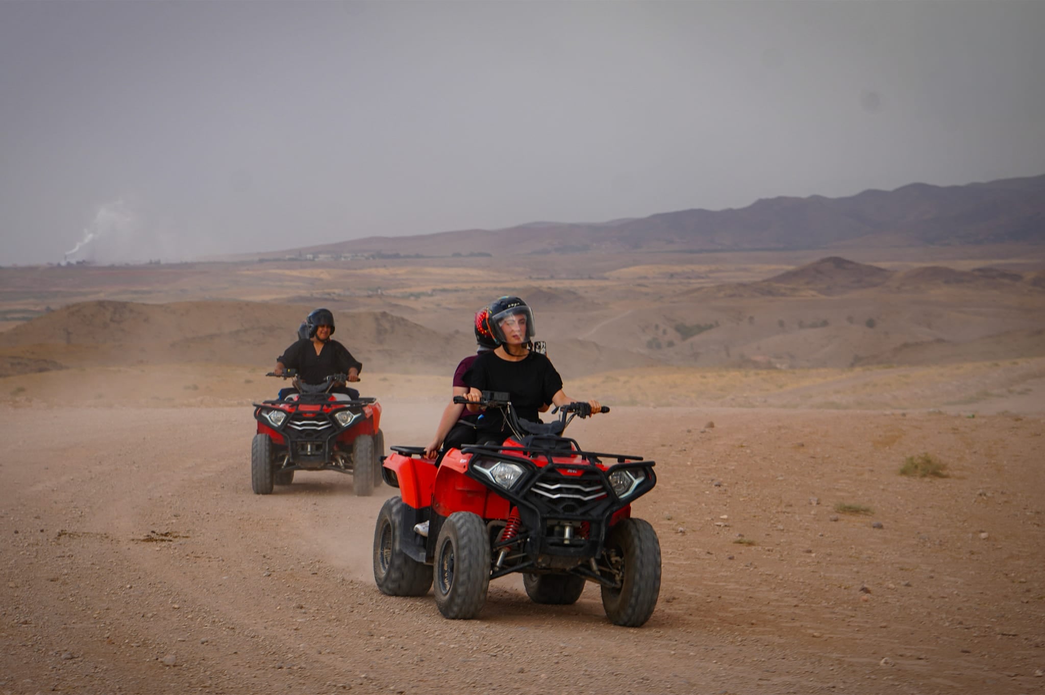 Due quad rossi avanzano verso l'obiettivo su una pista polverosa, montagne sullo sfondo